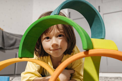 Lächelnder Junge spielt mit regenbogenförmigen Pyramide Spielzeug zu Hause - ELMF00133