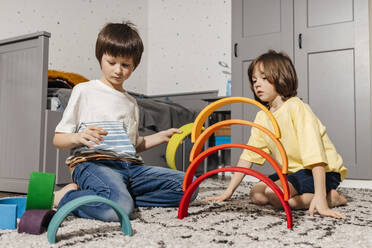 Boys, brothers play in the nursery with a wooden multi-colored rainbow and build a pyramid from it - ELMF00141