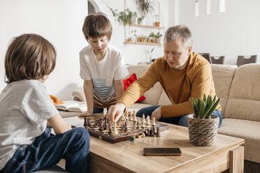 Father playing chess with children at home - ELMF00149