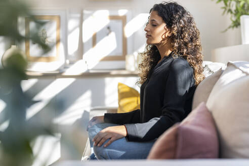 Woman meditating on sofa at home - JSRF02935