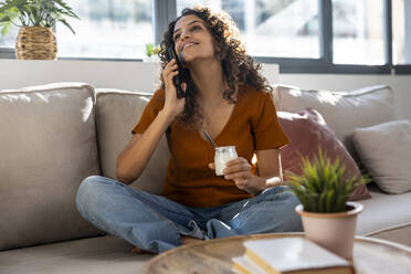 Smiling woman talking on smart phone sitting at home - JSRF02944