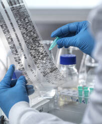 Genetic Research, Scientist holding a DNA sample and viewing an autoradiogram gel during an experiment in the laboratory. Genomics, medicine, cure, vial, new ideas, bespoke, tailor made healthcare, individual, DNA, electrophoresis gel, genetic finger print, DNA profile, genetics, biotechnology, biomedicine, biology, human DNA, DNA testing, genetic sequence, chemistry, future science, genome, analysis, vial, sample research, genome. - ABRF01165