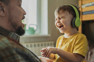 A little boy sits on his dad's lap and listens to music with headphones - ANAF02781