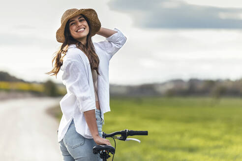 Glückliche junge Frau mit Fahrrad auf einem Feld - JSRF02953