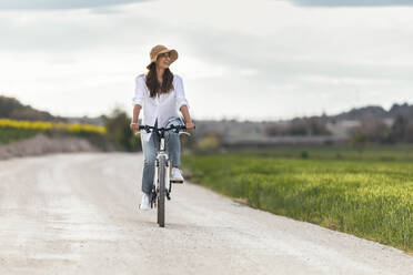 Glückliche Frau fährt Fahrrad auf der Straße unter bewölktem Himmel - JSRF02955