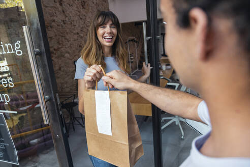 Glückliche Geschäftsfrau, die ein Lebensmittelpaket an der Bürotür erhält - JSRF02973