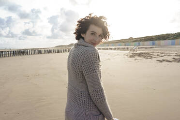 Lächelnde Frau in Strickjacke mit Blick zurück über die Schulter am Strand - KNSF10190
