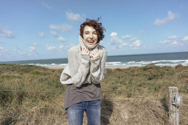 Verspielte Frau mit Rollkragenpullover am Strand stehend an einem sonnigen Tag - KNSF10201