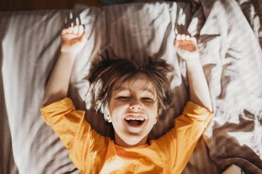 Portrait of a cute emotional boy with long hair in a bright orange sweatshirt at home - ANAF02797