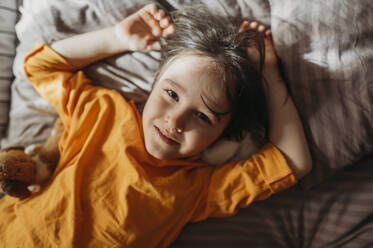 Portrait of a cute emotional boy with long hair in a bright orange sweatshirt at home - ANAF02800