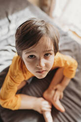 Portrait of a cute emotional boy with long hair in a bright orange sweatshirt at home - ANAF02808