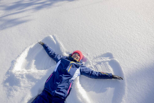 A smiling woman lies on the snow in winter on a sunny day. - MBLF00318