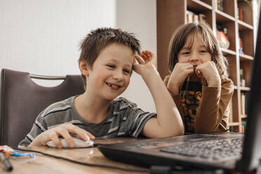 Two boys, brothers use a laptop while sitting at the table - ELMF00154