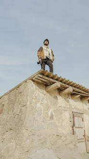 Ein Mann mit einer Kamera steht auf einem alten Gebäude in Bardenas Reales, Navarra, Spanien, vor einem klaren blauen Himmel. - ADSF54035