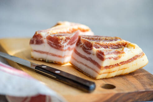 Thick, raw slices of lard placed on a wooden board, with a knife to the side, set for culinary uses. - ADSF54043