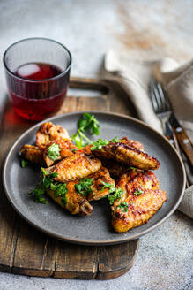 Delicious roasted chicken wings in a spicy sauce garnished with fresh coriander. Served on a grey plate with a cherry cocktail on the side. - ADSF54048