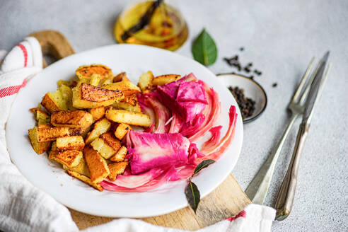 Ein lebhaftes Gericht aus pikantem fermentiertem Kohl mit Roter Bete, gewürzt mit Knoblauch und rotem Pfeffer, serviert mit gebackenen Kartoffeln auf einem weißen Teller. - ADSF54055