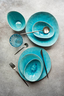 Top view of a stylish turquoise ceramic table setting with matching cutlery on a textured surface. - ADSF54058