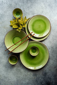 Top view of an elegant table setting featuring bright green ceramic dinnerware and wooden cutlery on a textured grey surface. - ADSF54063