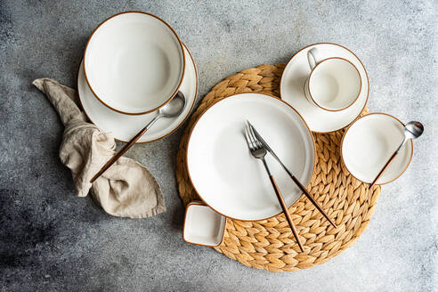 Draufsicht auf einen stilvoll gedeckten Tisch mit hellem Keramikgeschirr und elegantem Besteck auf einem gewebten Tischset, bereit für ein raffiniertes Esserlebnis. - ADSF54065