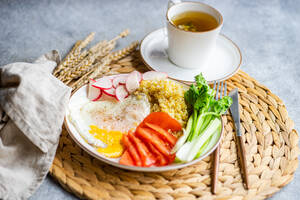 Ein nahrhaftes Mittagessen mit frischem Bio-Gemüse wie Rüben, Tomaten und Selleriestangen, begleitet von einem Spiegelei und Bulgur-Getreide, serviert mit einer Tasse duftendem Tee. - ADSF54072