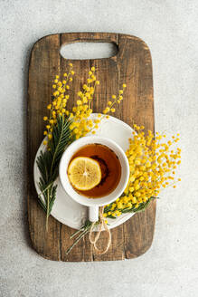 From above of inviting cup of tea with a lemon slice on a wooden board, adorned with fragrant Mimosa sprigs, captures the essence of a leisurely morning - ADSF54080