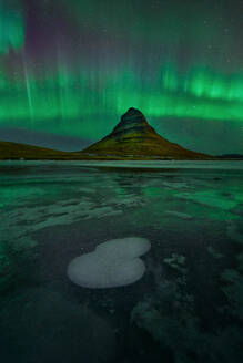 Magisches Schauspiel der Aurora Borealis, die den Nachthimmel über dem berühmten Berg Kirkjufell in Island erleuchtet, mit gefrorenem Vordergrund. - ADSF54088