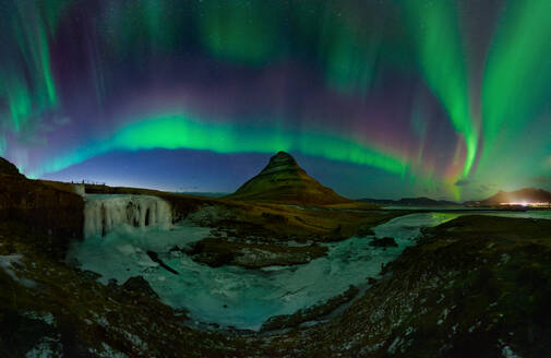 Aurora borealis tanzt über dem Berg Kirkjufell in Island, mit einem gefrorenen Wasserfall im Vordergrund. - ADSF54090