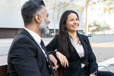 A man and woman in business attire share a light moment on a sunny day, reflecting a positive work environment. - ADSF54167