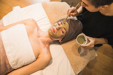 Eine Person genießt eine beruhigende Gesichtsbehandlung mit einer von einer Kosmetikerin aufgetragenen Tonerdemaske in einer ruhigen Spa-Umgebung - ADSF54186