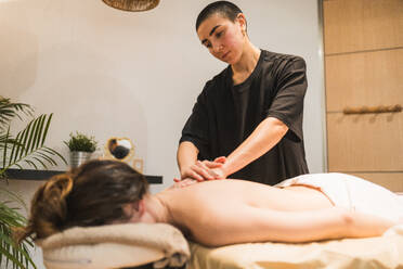 A skilled therapist provides a calming back massage to a client in a serene spa setting, promoting wellness and relaxation - ADSF54190