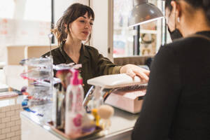 Eine freundliche Kassiererin unterhält sich mit einem Kunden an der Kasse eines modernen Ladens, der ein warmes und einladendes Ambiente bietet - ADSF54193