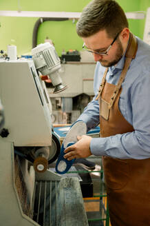 An attentive shoemaker in Austria is finely grinding a shoe sole on a machine, displaying craftsmanship and attention to detail. - ADSF54211