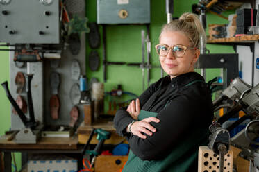 A proud female shoemaker stands in her workshop, surrounded by tools and shoe lasts, showcasing skill and tradition in her craft. - ADSF54216