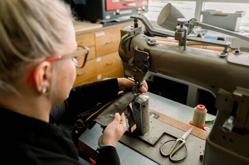 Ein verkürzter, nicht wiederzuerkennender Schuhmacher näht in einer gut ausgestatteten Werkstatt in Österreich mit einer Nähmaschine akribisch Leder zusammen und stellt dabei seine Handwerkskunst unter Beweis. - ADSF54218