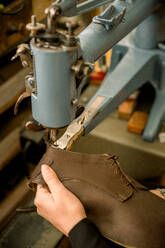 Close-up of a cropped unrecognizable shoemaker's hands stitching a leather shoe with a sewing machine in an Austrian workshop, showcasing traditional craftsmanship. - ADSF54219