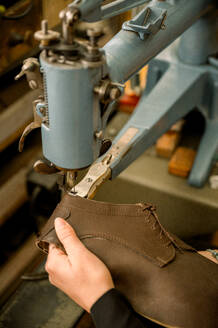 Nahaufnahme der Hände eines Schuhmachers, der einen Lederschuh mit einer Nähmaschine in einer österreichischen Werkstatt näht, wobei die traditionelle Handwerkskunst gezeigt wird. - ADSF54219