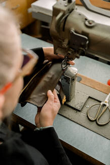 Ein unkenntlich gemachter Schuhmacher repariert in einer österreichischen Werkstatt mit einer Nähmaschine einen Lederschuh und zeigt dabei traditionelle Handwerkskunst. - ADSF54220
