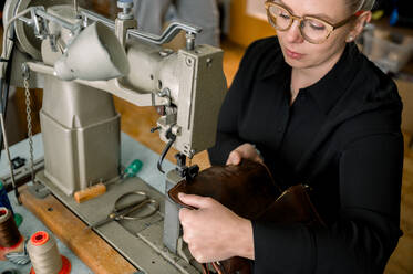Ein österreichischer Schuhmacher repariert sorgfältig einen Lederschuh mit einer Nähmaschine in einer gut ausgestatteten Werkstatt. - ADSF54221