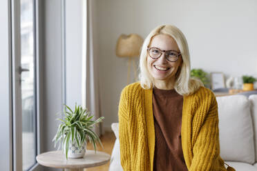 UAE, a woman in glasses in a yellow sweater sitting on a sofa by the window - TYF00823