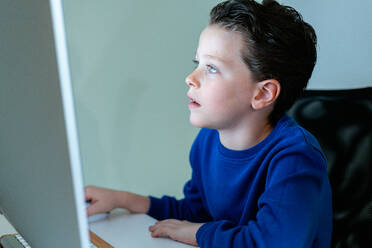 A young boy with a look of concentration while using a computer in a home environment, potentially engaged in online learning - ADSF54273