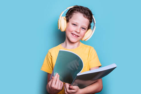 Ein charmanter Junge in einem gelben Hemd und mit Kopfhörern liest ein Buch und präsentiert eine Mischung aus Bildung und Technologie - ADSF54288