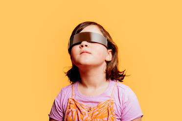 Junges Kind steht mit einem VR-Headset und schaut nach oben, isoliert auf einem hellen orangefarbenen Hintergrund - ADSF54303