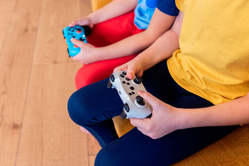 Ausgeschnittenes Bild von zwei Kindern, die mit bunten Controllern spielen, konzentriert auf ihre Hände und Geräte - ADSF54338
