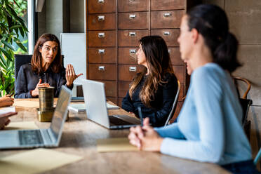 Drei berufstätige Frauen diskutieren während eines Geschäftstreffens in einem modernen Büro, das ein Beispiel für Teamwork und Zusammenarbeit in einem von Frauen geführten Unternehmen ist. - ADSF54356