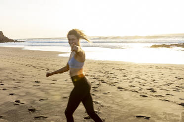 Eine energiegeladene Läuferin bewegt sich mit Freude am Ufer entlang, während die Sonne über dem Meer untergeht. - ADSF54362