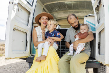 Eine fröhliche Familie mit zwei Kindern genießt die gemeinsamen Momente in einem klassischen Oldtimer-Van bei einem entspannten Outdoor-Abenteuer. - ADSF54383