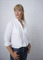 Beautiful natural blonde middle aged woman standing in front of white wall wearing white blouse and blue jeans - JBYF00270