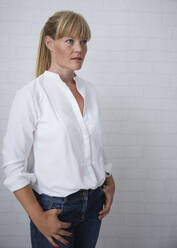 Beautiful natural blonde middle aged woman standing in front of white wall wearing white blouse and blue jeans - JBYF00271