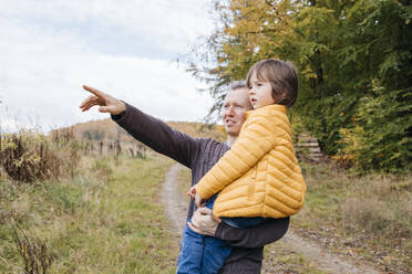 Dad holds his son in his arms in the autumn forest and points into the distance - ELMF00158